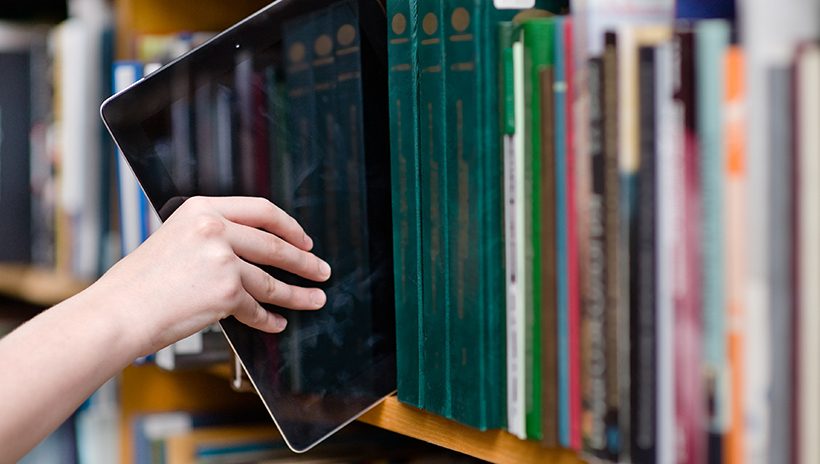 Student putting a tablet on a library book shelf