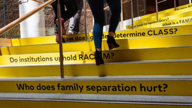Students climbing stairs with political questions on them (e.g., "Who does family separation hurt?")