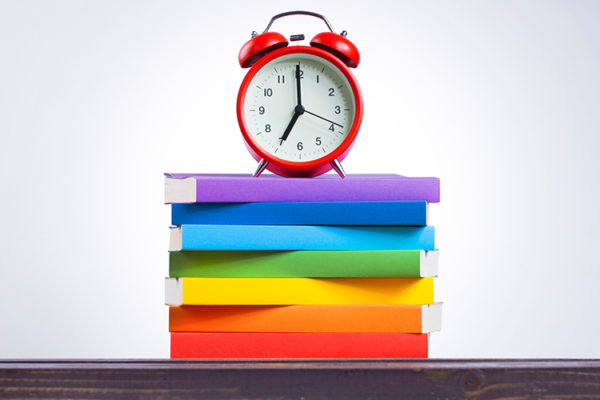 Rainbow-colored books with an alarm clock on top, representative of the need for LGBTQIA++ representation in library collections