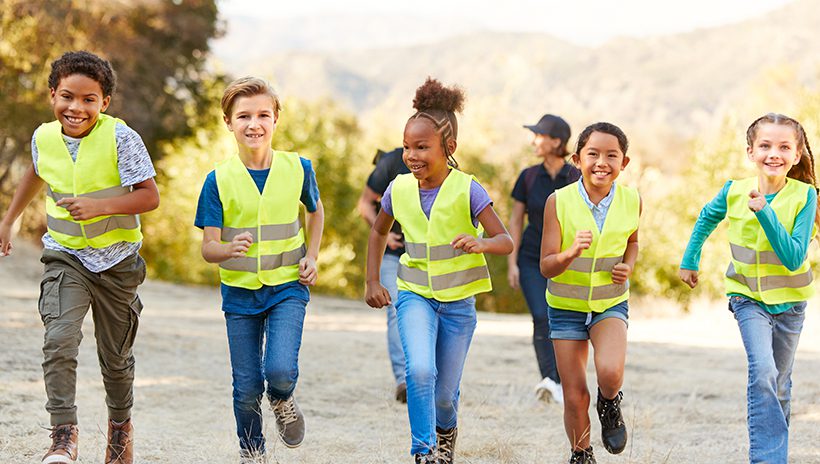 Five children running through field wearing reflective vests