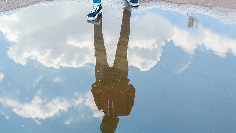 Teenage student looks at reflection in puddle