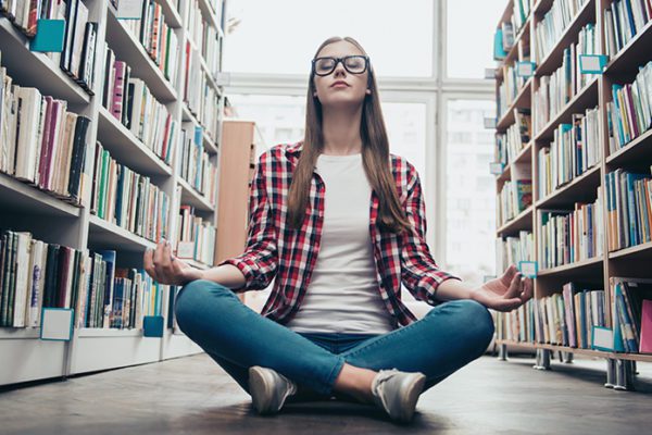 Female high school student meditating in library stacks